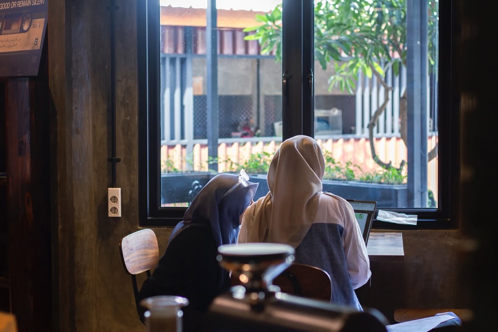 Dua pengunjung bekerja dengan laptop di dekat jendela